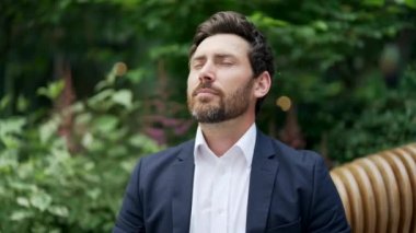 Yorgun, olgun sakallı adam mevsimsel alerjiden muzdarip. Yakın plan, takım elbiseli, üzgün bir erkek dışarıda bankta hapşırıyor. Sağlıksız çalışan kendini kötü hissediyor. Soğuk algınlığı veya grip yüzünden öksürüyor.