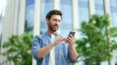 Neşeli işadamı mutlu bir okuyucu cep telefonundan harika haberler alıyor. Sıradan bir kutlama yapan iş adamı, şehrin dışındaki bir caddede ofis binasının yanında duran akıllı telefona baktı.