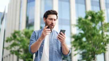 Yetişkin iş adamı, dışarıdaki şehir caddesindeki modern iş merkezinin yanında duran akıllı telefon ekranına bakarak kötü haber mesajı alıyor. Hüsrana uğramış üzgün adam