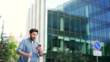 İş adamı toplantıya ya da ofiste çalışmaya geç kalır. Günlük giysiler içinde iş adamı telefona baktı ve şehir dışından ofis binasının yakınına doğru hızla koştu. Açık hava.