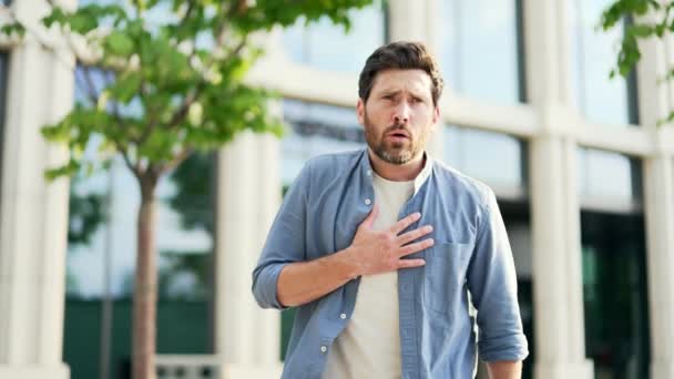 熟練した成熟した男性従業員は ビジネスオフィスセンター近くのベンチに座っている間 心臓の症状の心臓発作で強い突然の痛みに苦しんでいます ストレスを受けた男性は 腰痛を抱えています — ストック動画