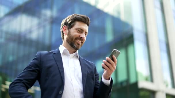 英俊的大胡子商人用手机 成熟的成年人一边站在办公区一边用智能手机聊天 一边发短信 社交网络技术人们 App — 图库视频影像