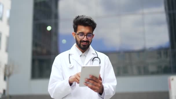 Χαμογελώντας Νεαρός Γιατρός Λευκό Παλτό Χρησιμοποιώντας Tablet Ενώ Στέκεται Έξω — Αρχείο Βίντεο