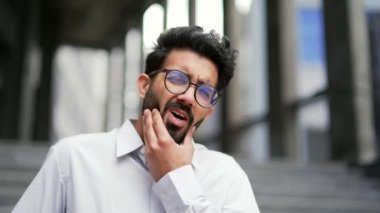 Kapatın. Genç bir işadamı bir ofis binasının yanında sokakta dururken diş ağrısı hisseder. Gözlüklü üzgün sakallı erkek, yanak yanağa acı çekiyor. Bir dişçinin yardımına ihtiyacı var.