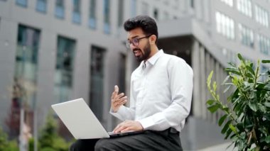 Genç işadamı, ofis binasının yanındaki bankta otururken bilgisayarla bir video görüşmesinde konuşuyor. Beyaz gömlekli, gözlüklü, gülümseyen yakışıklı bir adam bir arkadaşıyla internette sohbet ediyor.