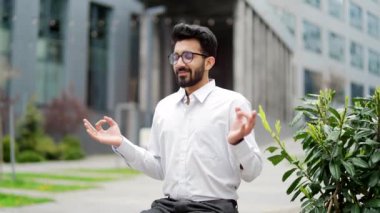 Beyaz gömlekli genç işadamı, kapalı gözlerle meditasyon yapıyor. Bir ofis binasının yakınındaki bankta oturuyor. Sakin bir işçi dinlenir ve huzuru hisseder. Erkek stres atmak için gevşer.