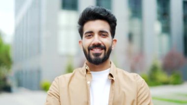 Kapatın. Gülümseyen ve kameraya bakan genç sakallı bir adamın portresi. Ofis binasının yanındaki sokakta poz veren yakışıklı bir erkek. İyimser iş adamının kafa resmi.