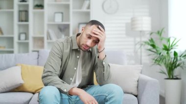 Evde, kanepede oturan üzgün, depresyondan muzdarip genç bir adam. Erkeğin zihinsel sağlık sorunları var. Endişeli, depresif bir adam evde migrenle, duygusal stresle boğuşuyor.
