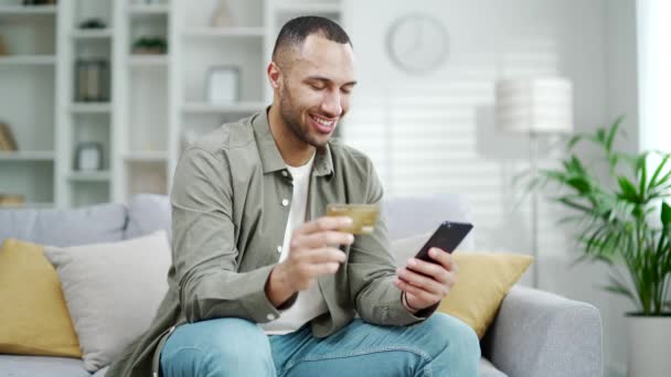 Młody Szczęśliwy Afrykański Amerykanin Siedzący Kanapie Korzystający Smartfona Zakupów Online — Wideo stockowe