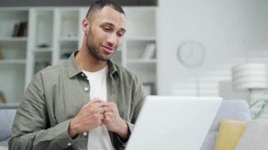 Yakışıklı adam evde video görüşmesinde konuşuyor. Webinar, online kurs, sanal toplantı sırasında. Modern oturma odasında çalışırken dizüstü bilgisayar kullanan çeşitli ırk siyah erkek özel ders hocaları