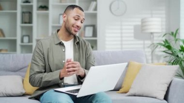 Yakışıklı adam evde video görüşmesinde konuşuyor. Webinar, online kurs, sanal toplantı sırasında. Modern oturma odasında çalışırken dizüstü bilgisayar kullanan çeşitli ırk siyah erkek özel ders hocaları