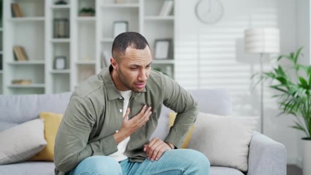 胸を抱える心臓の痛みを伴う混血した人種 心臓攻撃大人の男性は重度の胸痛を発症する 心筋梗塞について リビングルームに一人でソファーに座っている間の圧力 — ストック動画