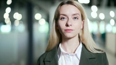 Kapatın. Modern bir ofiste duran gülümseyen genç bir iş kadınının portresi. Şık, mutlu, takım elbiseli kadın çalışan kameraya bakıyor. Başarılı bir yönetici veya girişimcinin vesikalığı
