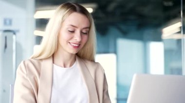 Kapatın. Modern bir ofisin çalışma masasında otururken dizüstü bilgisayarda yazan genç bir iş kadını. Bilgisayarda bir proje üzerinde çalışan sarışın bir kadın, bir müşteriye mesaj atmak ya da sohbet etmek.