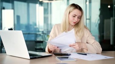 Modern ofiste iş yerinde otururken kağıt işlerinde zorlanan genç bir iş kadını hayal kırıklığına uğradı. Kafası karışmış sarışın kadın çalışan belgelere bakıyor ve sorunu anlayamıyor.