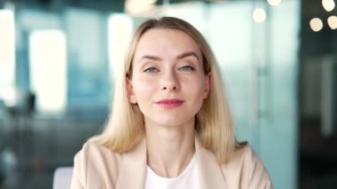Webcam görüntüsü. Yaklaş. İş kadını ofiste otururken kameraya bakarak video eğitimi alıyor. Sarışın kadın çevrimiçi çalışıyor, uzaktan bir kurs, webinar, ders veya seminer dinliyor.
