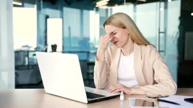 Ofiste çalışırken dizüstü bilgisayarla çalışırken göz yorgunluğu çeken aşırı çalışan sarışın iş kadını. Bir göz doktorunun önerdiği görüşü iyileştirmek için kadın göz ilacı enjekte ediyor