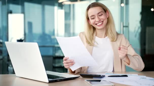 一位快乐的年轻女性金融家在办公室的办公桌前工作时 对自己正在审核的财务报告的结果感到满意 女商人对积极的指标感到满意 — 图库视频影像