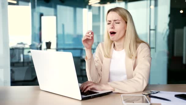 働き過ぎた若い女性の従業員は疲れを感じ 現代のオフィスの机の職場に座っている間 ラップトップで働くことを望んでいます 疲れ果てた女性は 目を閉じる 作業中のオーバーロード — ストック動画