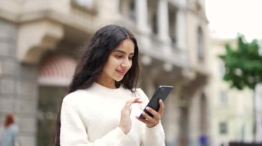 Genç bir kadın şehir caddesinde duran bir cep telefonu kullanıyor. Dişi öğrenci internette yazışıyor. Akıllı telefon uygulaması kullanıyor. Eski şehrin arka planında yaşam tarzı ve teknolojisi var.