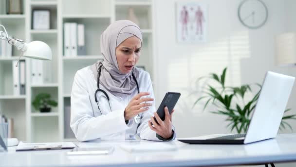可悲的穆斯林女医生坐在医院诊所时 在智能手机上看到了坏消息 医务工作者医生对不愉快的信息感到失望 结果是负面的 — 图库视频影像