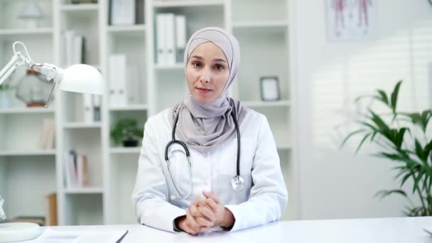 网络摄像头看到自信的穆斯林女医生在医院的诊所里听病人的视频电话 看着相机 医生在办公室里与医生交谈 向医生咨询意见 — 图库视频影像