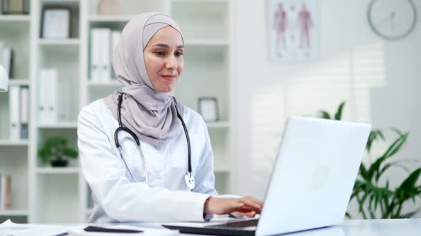 穆斯林女医生在诊所的笔记本电脑上打字 计划研究 阅读网上报告 在医院从事计算机 医学分析和远程保健工作的快乐女性 — 图库视频影像