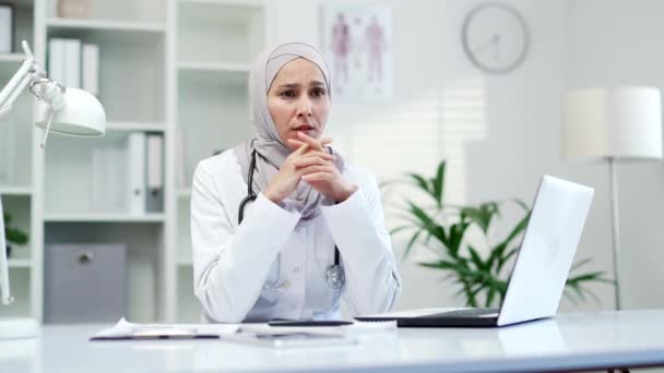 患疲倦和头痛的抑郁的穆斯林女医生 坐在医院诊所的工作场所 疲惫的女性医务工作者 正在经历悲伤或烦恼的女性医务工作者 — 图库视频影像