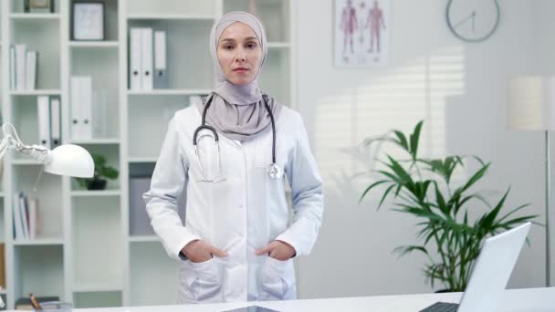 现代医院门诊部中穿着白衣 头戴听诊器的自信女医生的画像 穆斯林女医务工作者摆出一副站在办公室里的架势 — 图库视频影像