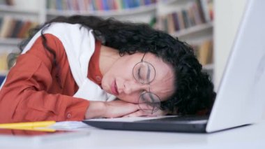 Kapatın. Kampüs kütüphanesinde laptopun arkasında uyuyan çok çalışan kız öğrenci. Sınavda öğrenmekten yorgun düşmüş bir kız. Yorgun bir aday giriş sınavları için hazırlanıyor
