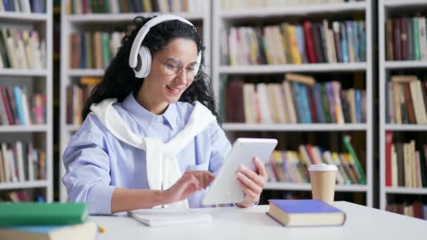 Kulaklıklı Kız Öğrenci Kampüs Kütüphanesinde Otururken Öğrenmek Için Tablet Kullanıyor — Stok video