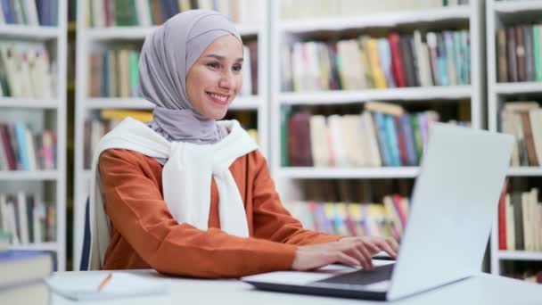身穿头巾的穆斯林女学生坐在校园图书馆的书桌前 在笔记本电脑上工作 女生在考试期间用电脑浏览 核对作业或准备考试 — 图库视频影像