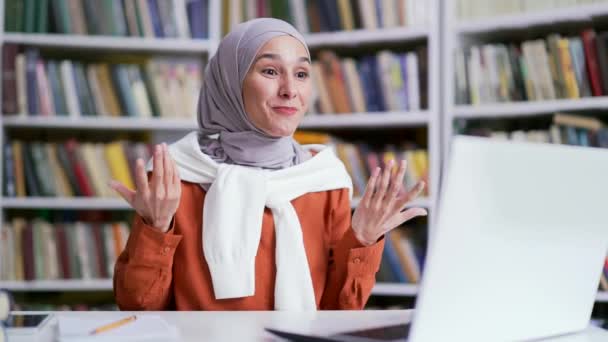 戴头巾的穆斯林女学生在图书馆用笔记本电脑通过视频电话听在线电子学习与教练交流 老师对学生进行培训 远程授课 — 图库视频影像