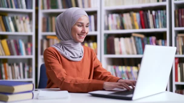 ヒジャーブのムスリム女性学生は キャンパス図書館の机に座っている間 ノートパソコンで働いていました 女の子は コンピュータを使用します タイプ 宿題をチェックしたり 試験期間中に試験の準備 — ストック動画