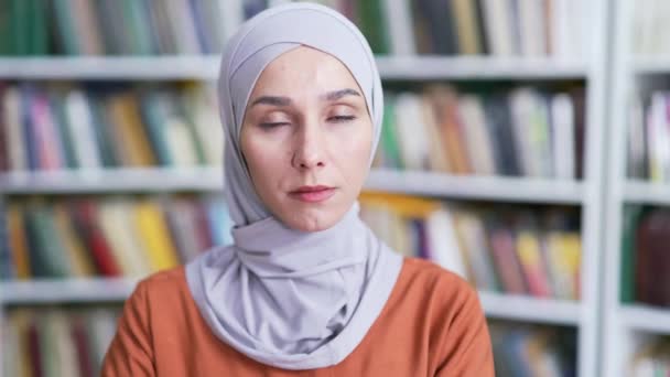 靠近点穿着头巾站在校园图书馆空间的自信的穆斯林女学生的画像 一个可爱而严肃的女孩正在看着摄像机 在教室里摆姿势的时髦申请者的头像 — 图库视频影像