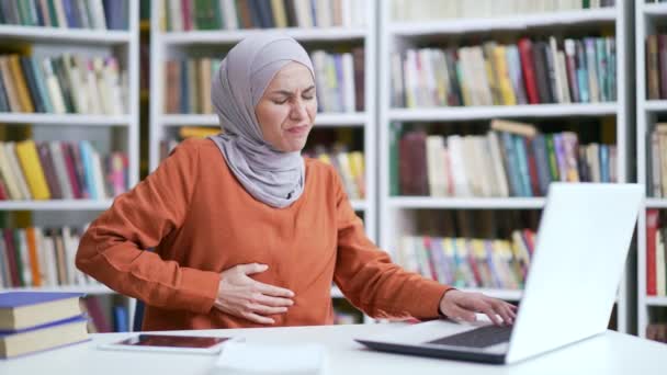 穆斯林女学生在校园图书馆的笔记本电脑上工作时 会感到胃痛 女孩有消化 胃溃疡 便秘或月经等问题 — 图库视频影像