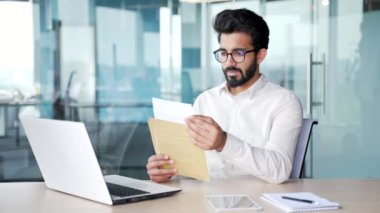 Modern ofisteki çalışma masasında oturmuş harika haberlerle mektup okuyan mutlu genç işadamı. Bir adam başarıyı kutluyor, keyifli bir haber almaktan mutluluk duyar. Vay canına.