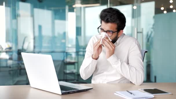 病気のビジネスマンは 現代のオフィスで職場に座っている間 ノートパソコンで働いている間 鼻水に苦しんでいます 悲しい男性はハンカチで鼻を拭く ひげ付きの男は風邪 ウイルスまたはインフルエンザを持っています — ストック動画