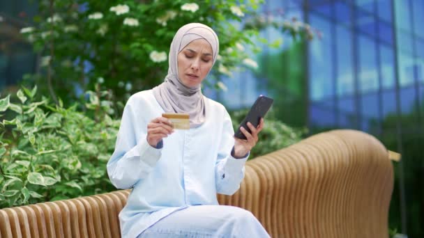 Zdenerwowany Muzułmański Pracownik Hidżabie Trzymający Kartę Kredytową Patrzący Telefon Siedzący — Wideo stockowe