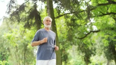 Yaşlı, gri saçlı, sakallı bir koşucu şehir parkında koşuyor ve akıllı bir saat gibi görünüyor. Olgun, formda bir erkek, fitness takip cihazı kullanıyor ve sonuçları kontrol ediyor. Doğada antrenman yapan yaşlı sporcu.