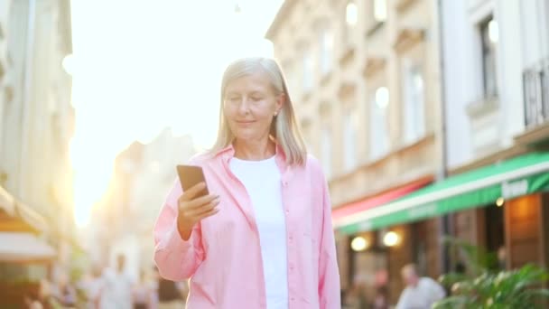 Mujer Pelo Gris Senior Utiliza Teléfono Inteligente Mientras Camina Por — Vídeo de stock