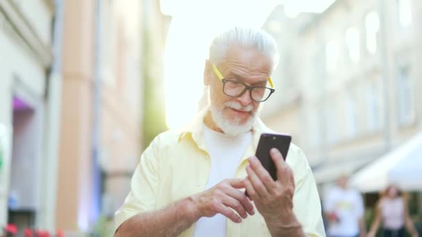 在一个站在城市街道上的智能手机上的视频通话中 一位头发灰白的大胡子老人听到了这个好消息 快乐的笑着 穿着一件衬衫的成熟的老男人表现出肯定的手势哇哦效果 — 图库视频影像