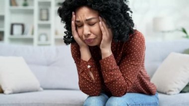 Kapatın. Genç üzgün Afrikalı Amerikalı kadın evdeki kanepede otururken depresyona giriyor. Sorunlarını düşünen yalnız siyah bir kadın. Yorgun, mutsuz, hayal kırıklığına uğramış ve kötü bir ruh hali var.