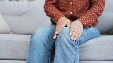 Kapatın. Oturma odasındaki kanepede otururken kadın elleri diz kaslarına masaj yapıyor. Üzgün siyah kadın diz eklem ağrısı çekiyor, yürüyemiyor, hastalık, kramp, romatizma.
