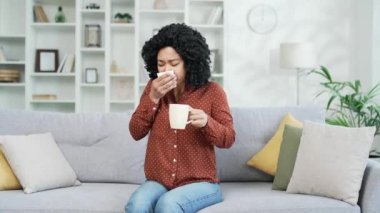 Hasta Afrikalı Amerikalı kadın evdeki oturma odasında kanepede otururken öksürüyor. Soğuk algınlığı, virüs, bronşit ya da grip. Yorgun siyah kadın burnunu mendille siler ve çay içer.