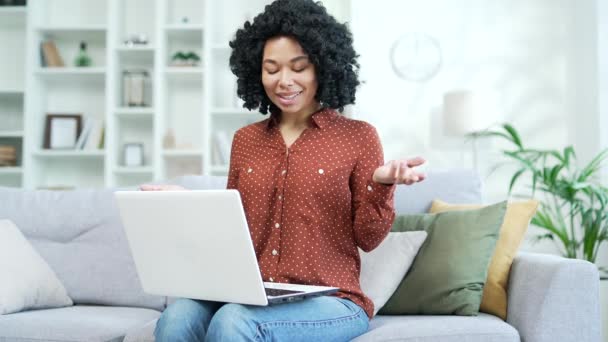 年轻的非洲裔美国女商人坐在总公司的沙发上 用笔记本电脑对着一个视频通话 黑人女性自由职业者在网上交流 网络研讨会 与客户进行咨询 — 图库视频影像
