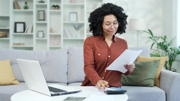 忙碌的年轻非洲裔美国女会计师坐在总公司做文书工作 有信心的黑人女性金融家在计算器 笔记本笔记 笔记本电脑上的类型上进行计算 — 图库视频影像