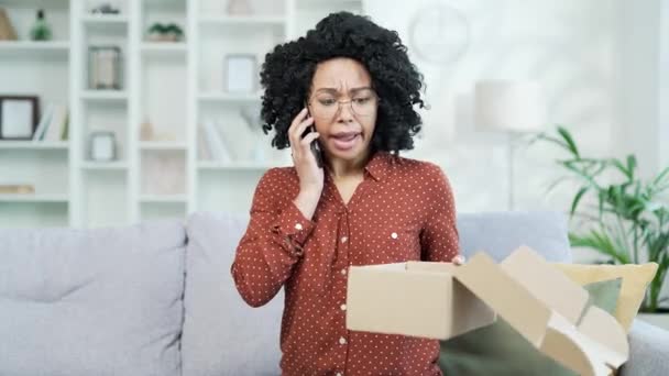 不幸なアフリカ系アメリカ人女性が 自宅で間違った商品を手に入れた後 電話で主張した 黒人女性は悪いレビューをしているが 彼女はオンラインストアで買い物をすることに不満を抱いている 破損したアイテム — ストック動画