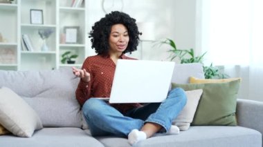 Genç Afro-Amerikan kadın, video görüşmesinde merkez ofisteki kanepede dizüstü bilgisayar kullanarak konuşuyor. Siyahi kadın öğrenci çevrimiçi bir toplantıda iletişim kuruyor, özel hocasıyla görüşüyor.