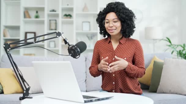 年轻的非洲裔美国女性带着话筒坐在家里的办公室里 正在用笔记本电脑录制播客 黑人妇女通过视频通话 远程采访或网络研讨会进行在线交流 — 图库视频影像